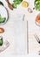 White cutting board on kitchen table background with Healthy food ingredients and tools, top view, frame. Clean eating and cooking