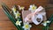 White daffodils and brown gift box, greeting card with pink ribbon on wooden background 4K video.Female hand puts flowers