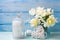 White daffodils and tulips flowers in blue vase, candles and d
