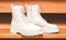 White demi-season boots made of eco-leather with fasteners, laces and rough sole on wooden steps.