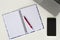 White desk with laptop keyboard, open colourful notebook, red pen and mobile phone. Flat lay, top view