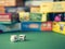 White dice on the green surface on the blurred background of colorful board game boxes