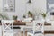 White dining room interior with posters and chairs at wooden table with flowers. Real photo