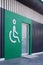 White disabled wheelchair sign with glass door on green wall and wooden panel wall decorations in public restroom