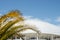 A white domed building behind a palm tree branch against the blue sky. Selective focus. Copy space