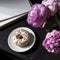 White donut with colored dusting on saucer and a couple of peonies on a table