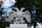 White doubleheaded metal eagle standing on the Park gate, against the background of trees and
