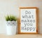 White drawing board with the phrase do whats makes you happy written on it against textured wall