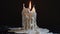 a white dripping candle, its flame casting a warm glow against a dark background, leaving trails of wax as it slowly