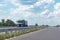 A white dump truck drives out of town on a flat asphalt road among fields against a blue sky with clouds on a sunny day