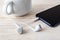 White earphones and smartphone near cup on a white wooden table. Modern personal device with touchscreen for music and