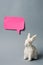 White Easter bunny with pink sticky note on gray background decoration animal Copy Space