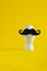 White egg with black moustache in ceramic egg cup on yellow empty background with copy space, concept for easter, breakfast, male