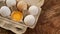 White eggs carton and cracked egg half with yolk top view on wooden background