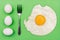 White eggs, fork and fried egg on a green background. Morning breakfast concept