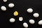 White eggs lie scattered on a black background. One egg is broken and the yolk is visible. Minimalistic design and color trend