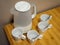 White electric kettle and four white ceramic mugs with teaspoons on wooden table