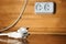 White electric plug lying on a floor with a socket on the wooden wall on the background