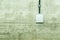 White electrical power outlet with cover cap and black cable attached on grunge concrete wall.