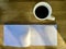 White empty page of paper with hot black coffee in cup on wood surface with early morning sunlight