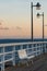 white empty wooden bench on pier by sea or ocean water, tranquility and serenity concept, calm sunset scene