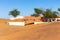 White entry gate buried in sand in Al Madam ghost village, with sand dunes and wild ghaf trees