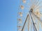 White ferris wheel attraction illuminated with bright white lights against clear blue sky on a sunny summer day. Entertainment on