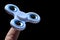 White fidget spinner toy balancing on tip of index finger of adult male person, black background