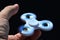 White fidget spinner toy rotating on index finger of adult male person, black background