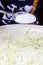 White fine salt in a tablespoon above metal bowl with shredded cabbage close-up