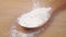 White flour falls on a wooden spoon on a cutting board close up.