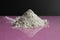 white flour of the highest or first grade lies in a heap on a black and pink fuchsia mirror background with a reflection side view