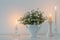 White flowers in white ceramic vase with burning candles in white interior