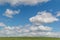 White fluffy bright clouds in blue sky with green grass field, open space