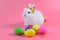 White fluffy rabbit wears a golden crown sitting on pink background and colourful egg
