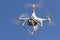 White flying dron with camera on blue sky background