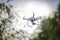 White flying quadrocopter with camera on green forest background