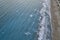 White foamy sea waves splash to sandy beach in the evening. Evening surf. Aerial top view from UAV drone