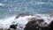 White foamy waves splashing over rocks on the beach in slow motion, close up.