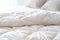 White folded duvet lying on white bed background. Preparing for winter season, household, domestic activities, hotel or