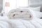 White folded duvet lying on white bed background. Preparing for winter season, household, domestic activities, hotel or