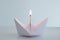 White folded paper boat with a match on fire on top frontal shot isolated on bright background