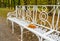 White forged bench in autumn park with abandoned maple leaves