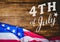 White fourth of July graphic against wood table and american flag