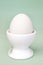 White fresh egg in ceramic light eggcup stand on blue background macro