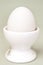 White fresh egg in ceramic light eggcup stand on blue background macro  retro style