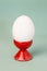 White fresh egg in ceramic red eggcup stand on blue background macro