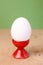 White fresh egg in ceramic red eggcup stand on wooden and green background macro