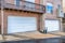 White garage door of house under balcony overlooking wet driveway and road