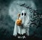 White ghost holding a carved pumpkin with candies in Halloween.